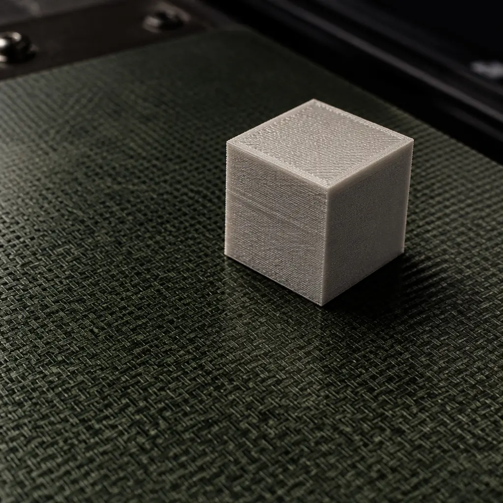 G10 Garolite fiberglass-epoxy build plate with a freshly printed nylon (PA6) calibration cube — the matte black surface texture visible at macro level, showing the distinct weave pattern of the laminate and the clean release surface
